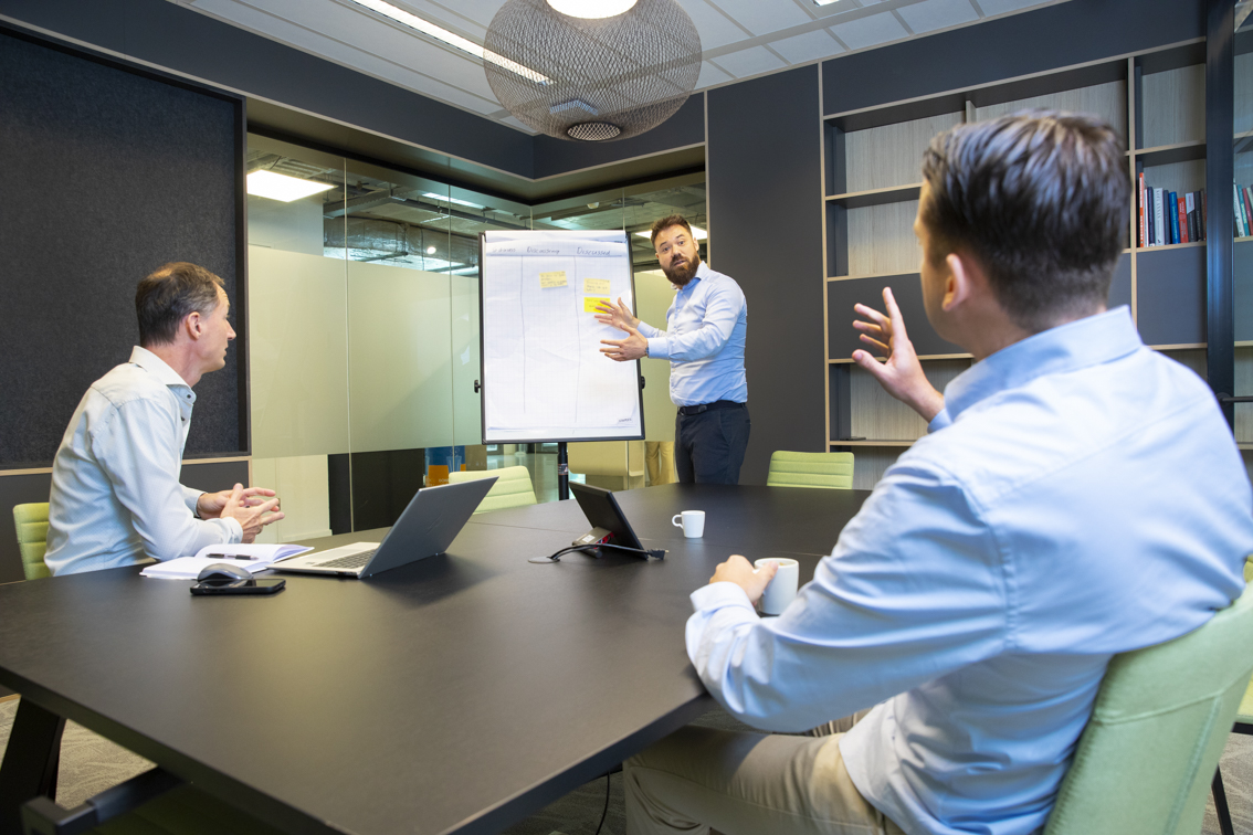 Collega van Het Normo team die voor een flipover staat en iets verteld aan twee collega's